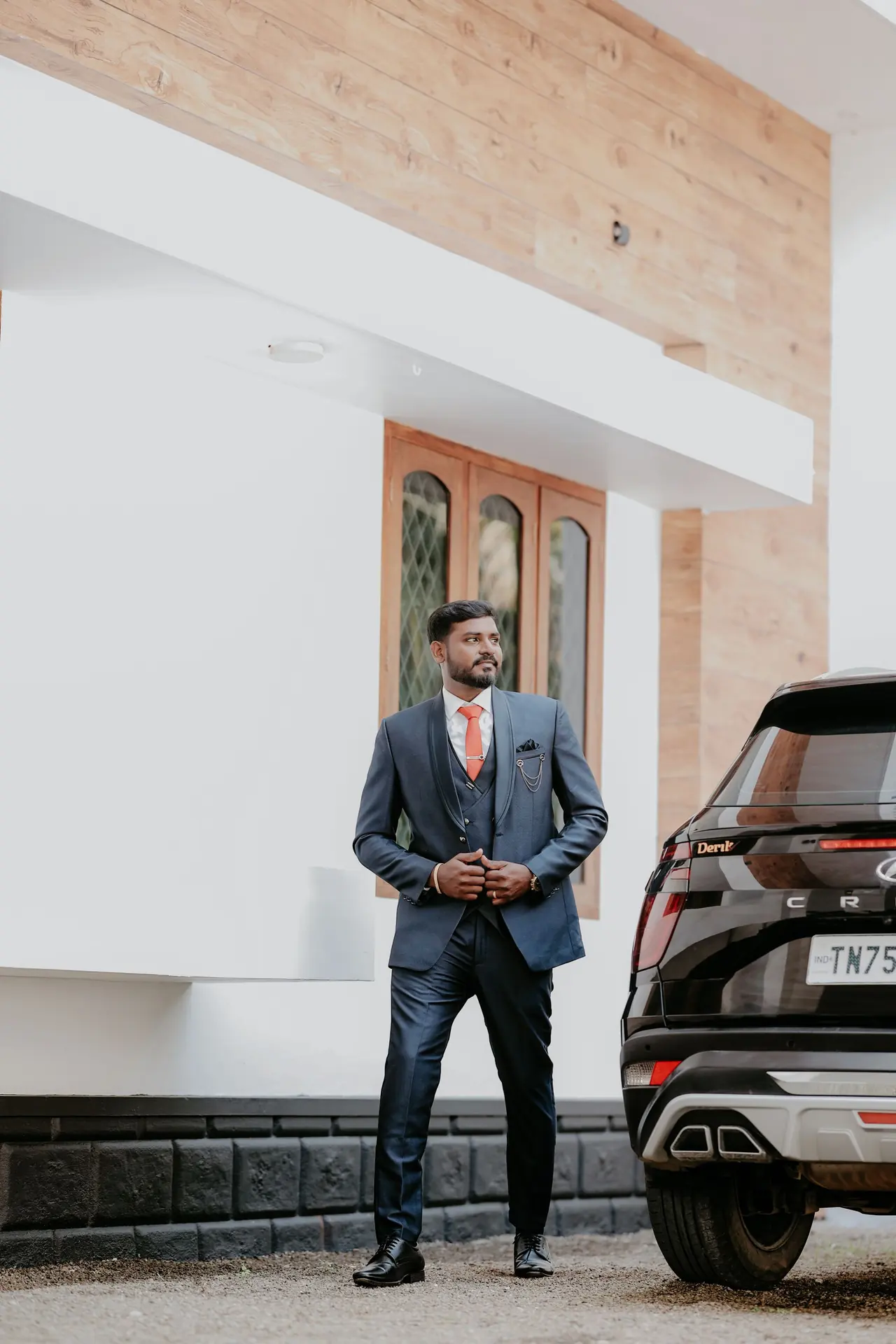 A man in a suit standing beside a clean dark SUV on a driveway.