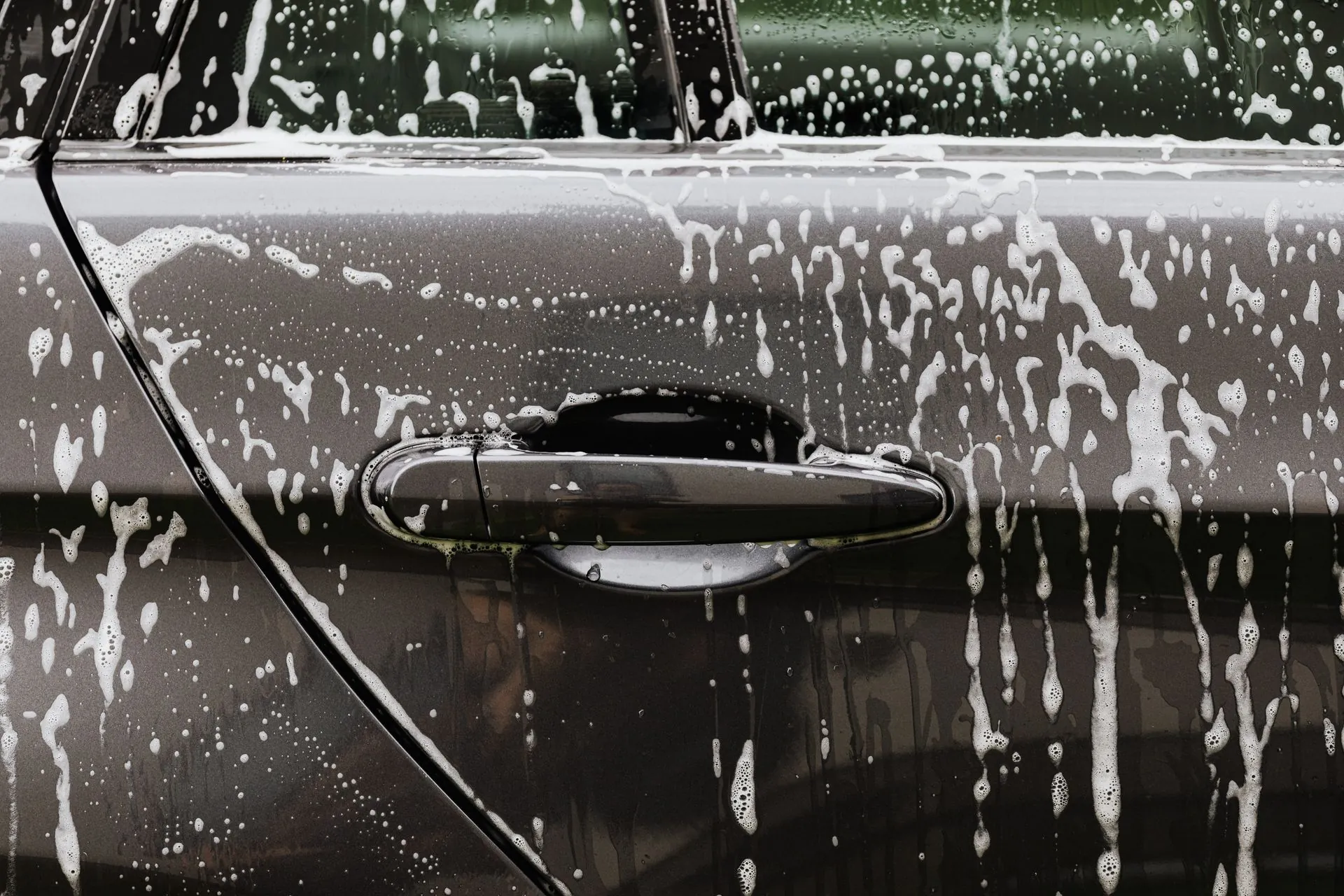 Snow foam running down the door of a dark car in the wash bay.