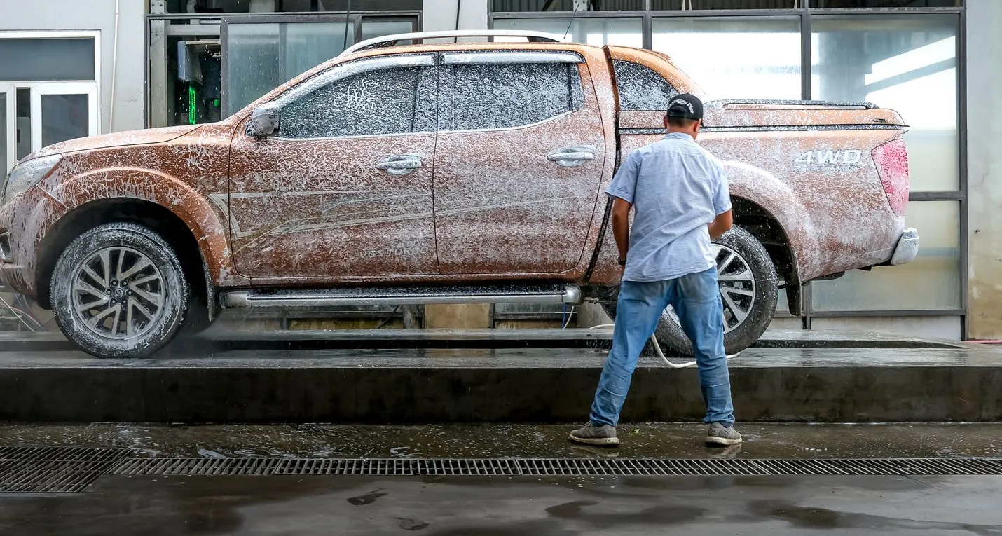 A pickup covered in snow foam being rinsed down by hand in a wash bay.
